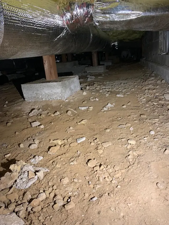 Bare, debris-covered crawl space soil before the barrier