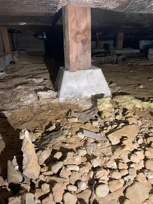 Crawl space with loose rock and debris around a support post