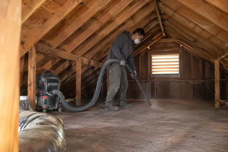 A technician vacuums the attic floor.