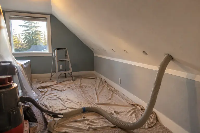 Blowing dense-pack cellulose into the sloped ceiling of a finished attic room.