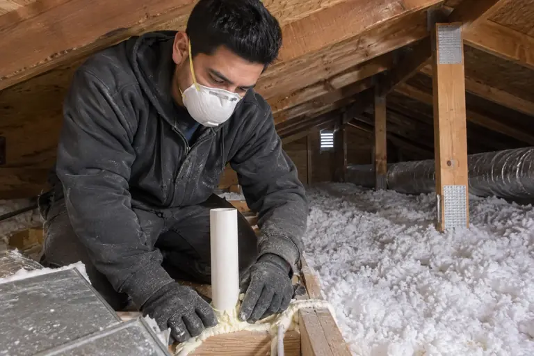 A technician inspects and air seals top plates and duct penetrations in a well-maintained Craftsman bungalow attic.