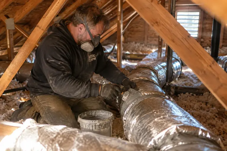 A technician seals duct connections with mastic in an attic.