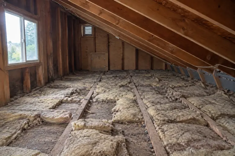 Attic insulation upgrade in Rainier Beach, before: The attic floor with worn, patchy batt insulation clearly showing gaps and compressed areas before the upgrade work begins.