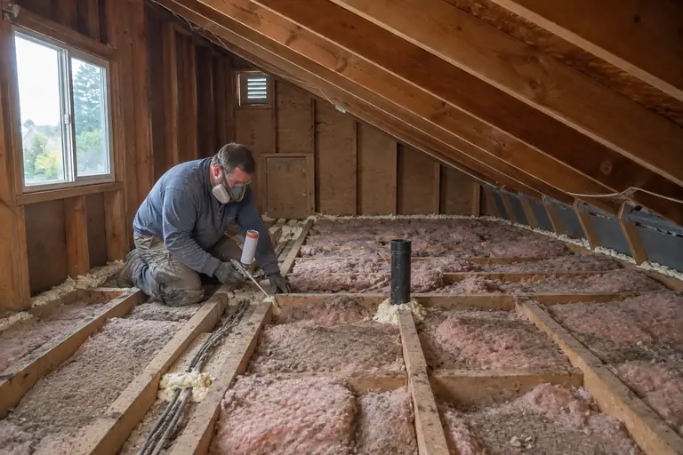 Attic insulation upgrade in Rainier Beach, in progress: Sealing air leaks in the attic floor joists using expanding foam to improve overall insulation effectiveness.
