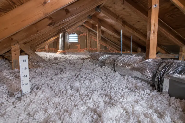 Fresh blown-in insulation and sealed ducts in an attic, with a depth ruler.