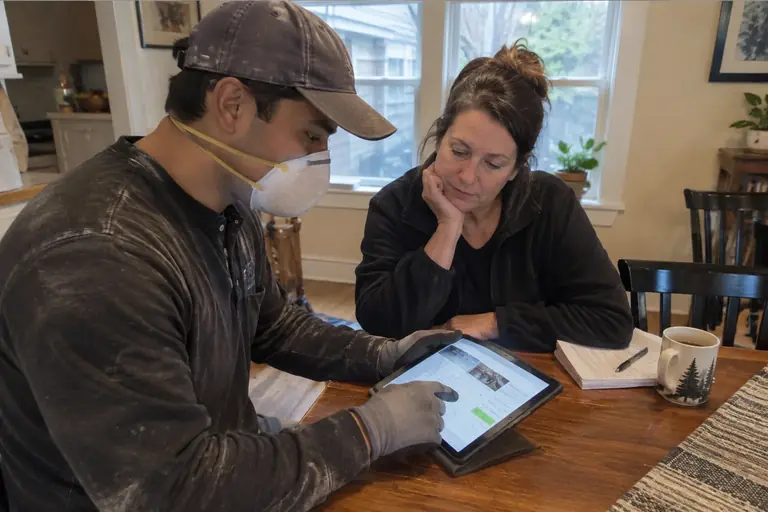 Technician and homeowner review a detailed attic insulation upgrade quote on a tablet.