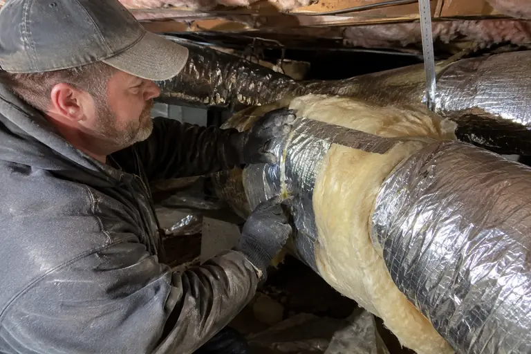 Technician carefully installs R-11 duct wrap insulation in a crawl space.