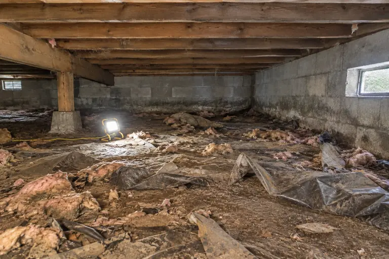 Crawl space cleaning with debris and vapor barrier removal in Bellevue, in progress: A technician carefully removes the old torn vapor barrier material from the dirt floor, clearing debris to prepare the space for cleaning.