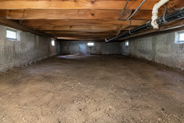 Crawl space cleaning with debris and worn vapor barrier removal in Olympia rambler, after: Finished cleaning: the crawl space floor is cleared completely of debris and torn vapor barrier, revealing the bare dirt floor and clean joists.