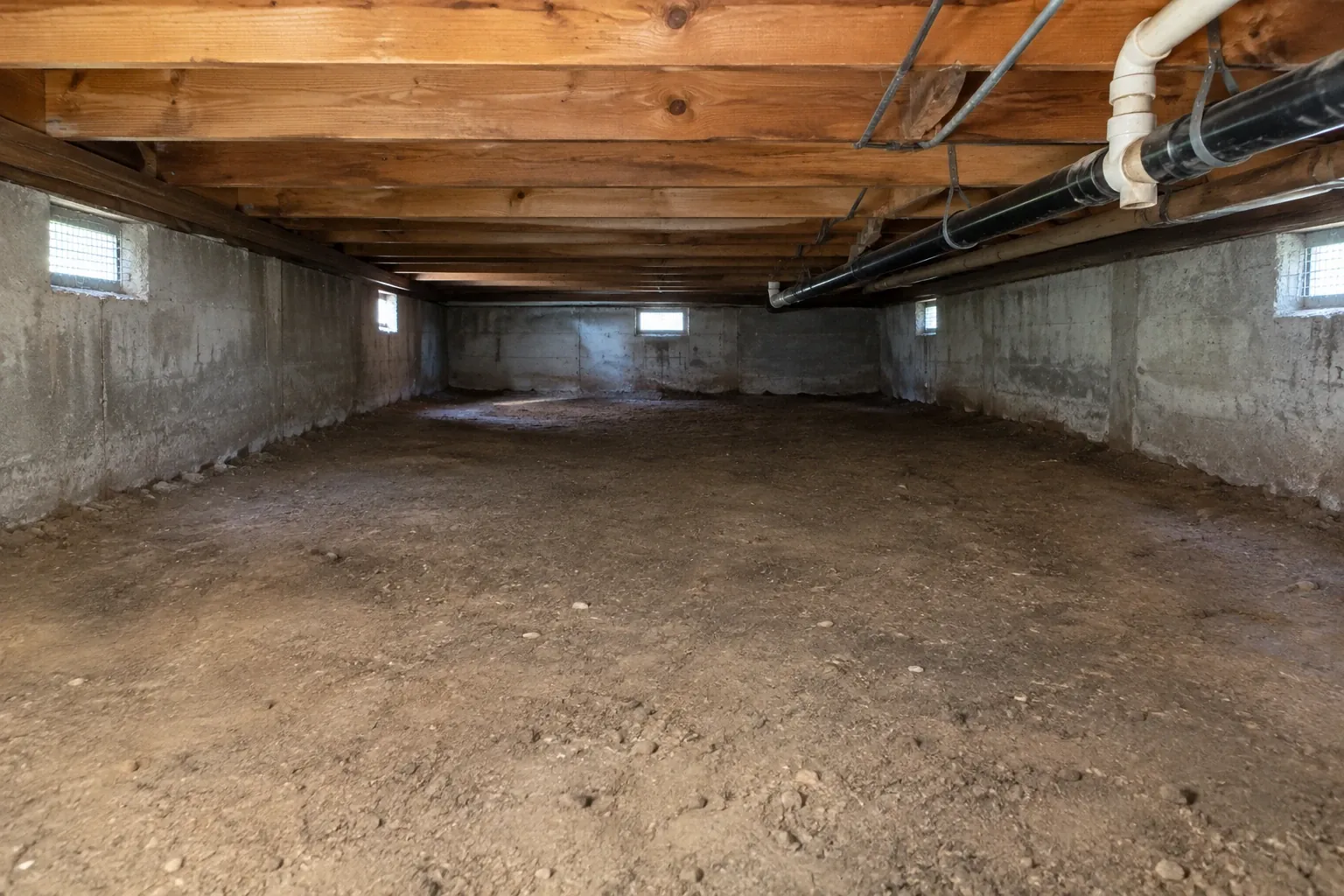 After: Finished cleaning: the crawl space floor is cleared completely of debris and torn vapor barrier, revealing the bare dirt floor and clean joists.