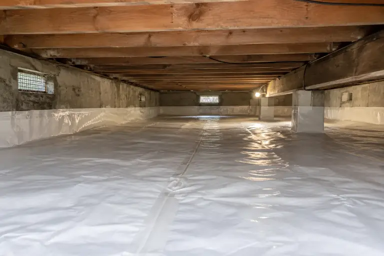 Crawl space cleaning with debris-strewn dirt floor, after: The crawl space liner is fully installed, creating a clean and sealed environment that protects against moisture and pests.