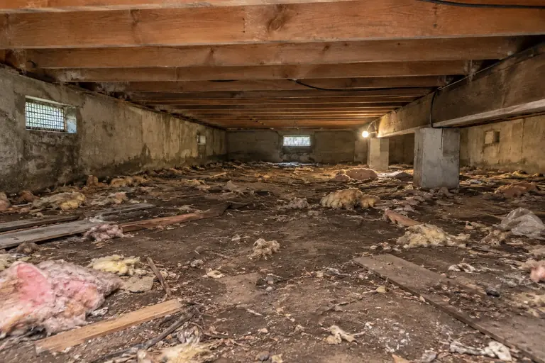 Crawl space cleaning with debris-strewn dirt floor, before: The crawl space floor is covered in debris and old insulation remnants, making the area appear dirty and neglected.