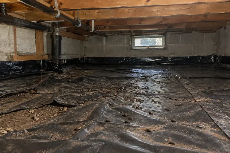 Crawl space cleaning with rodent droppings removal and barrier resealing, before: Before cleaning, the crawl space floor liner is heavily soiled with rodent droppings and partially displaced, posing a hygienic concern.