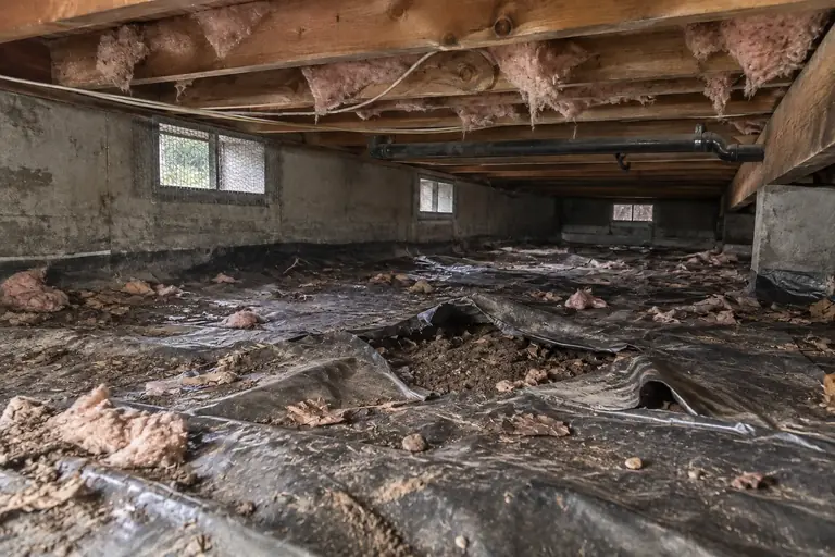 Crawl space cleaning with torn black poly removal and replacement, before: The crawl space is shown before work, with the old black polyethylene vapor barrier torn and damaged, exposing dirt and debris below.