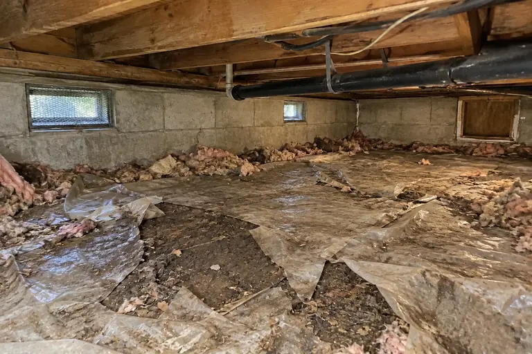 Crawl space cleaning with worn vapor barrier in Tacoma ranch, before: Before cleaning, the crawl space floor’s vapor barrier is heavily worn, torn, and dirty, with debris and exposed damp soil clearly visible.