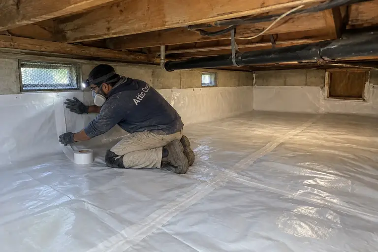 Crawl space cleaning with worn vapor barrier in Tacoma ranch, in progress: A technician installs and secures a new moisture barrier, taping seams and fastening edges to the foundation walls.