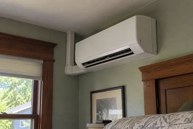 A ductless mini-split heating and cooling head is installed in the bedroom of an older Craftsman home.