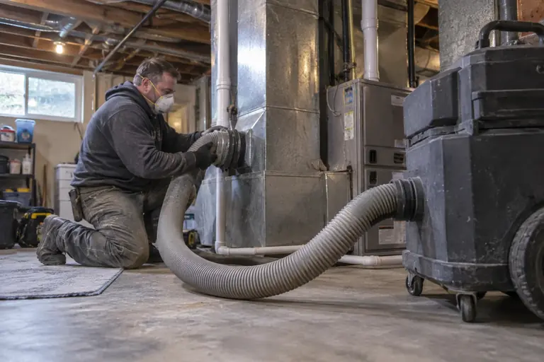 A technician connects a negative-air machine to a duct trunk.