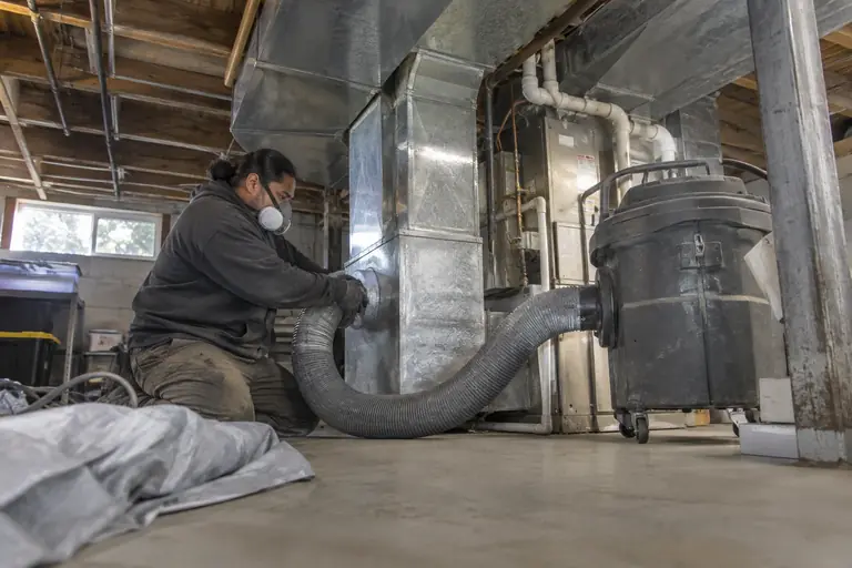 A technician connects a vacuum hose to a duct trunk.
