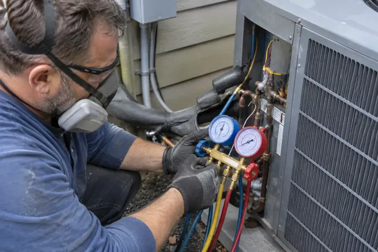 A technician in protective gear is carefully commissioning a heat pump using pressure gauges in a Seattle home.