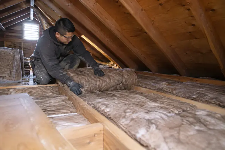 A technician installs EcoBatt insulation between attic joists.
