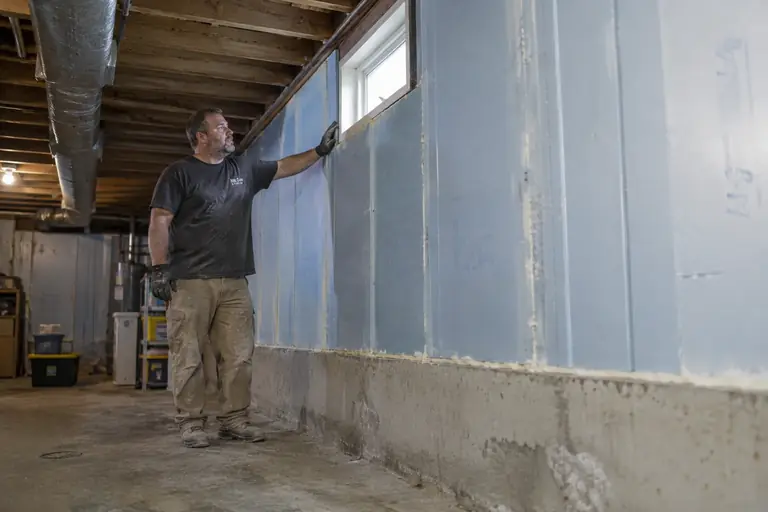 A technician installs rigid foam board on a basement wall.