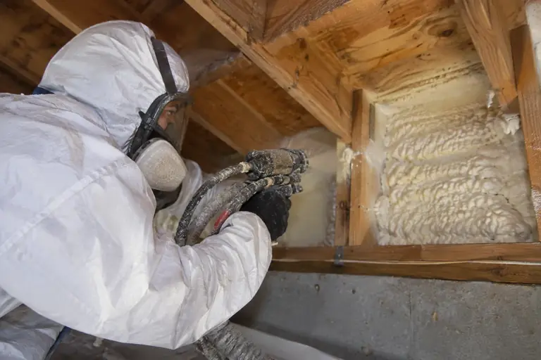 A technician sprays foam insulation into a wall cavity.