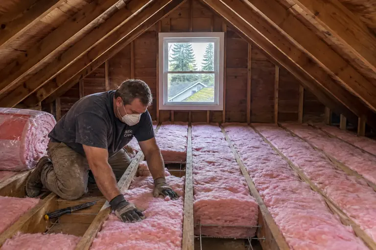 Attic insulation replacement in a Seattle Craftsman bungalow attic, in progress: The insulation installation continues as the batts are carefully fitted and secured tightly to ensure thorough coverage.