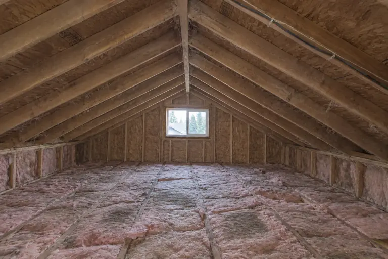 Attic spray foam insulation replacement in mid-century rambler attic, before: This mid-century rambler attic shows worn fiberglass batt insulation with gaps and damage diminishing energy efficiency.