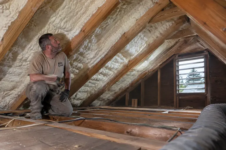 Final inspection of attic spray foam insulation installation with visible open-cell foam above ceiling joists.