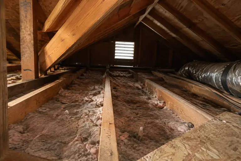 Old, compressed attic insulation is seen below the joist tops in a typical Seattle Craftsman home, showing wear and reduced effectiveness.