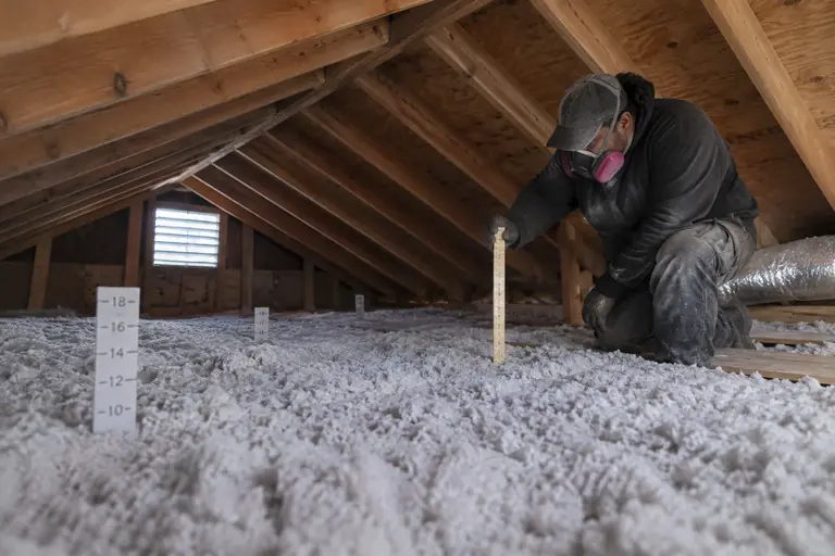 Technician measuring the depth of new attic insulation using a ruler to ensure proper installation for energy efficiency rebates.