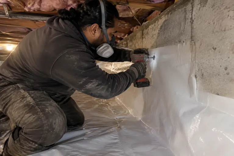 A technician fastens a white moisture barrier to the foundation wall.