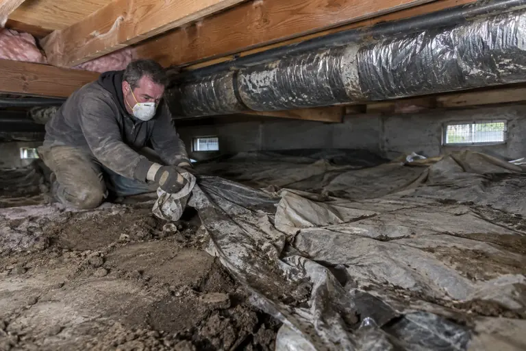 A technician pulls up an old, torn vapor barrier.