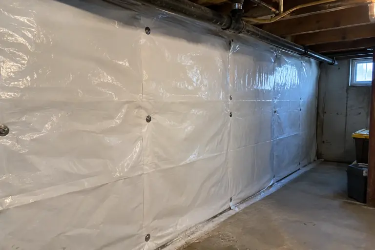 A white vapor barrier installed on a basement wall.