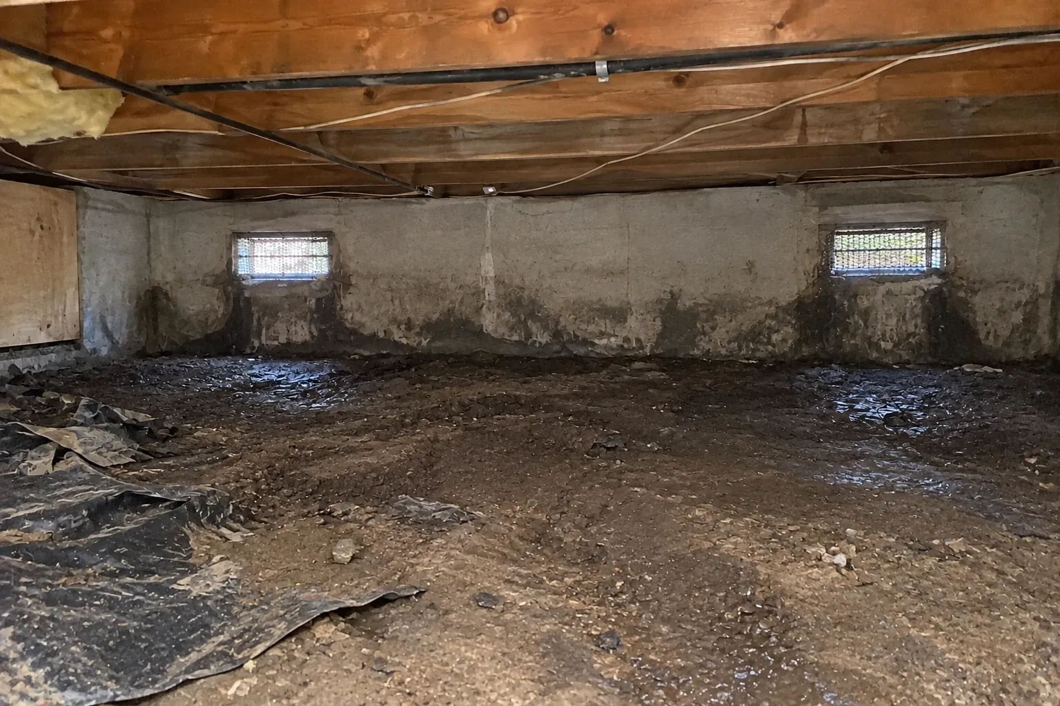 Before: The crawl space floor is bare and damp, with torn plastic debris and moisture clearly visible under the vents.