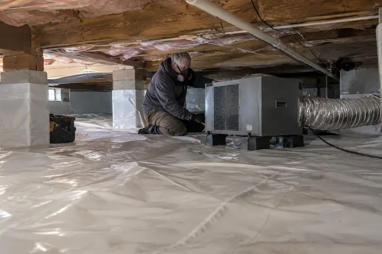 Technician installs and operates a crawl space dehumidifier on a freshly sealed vapor barrier liner.
